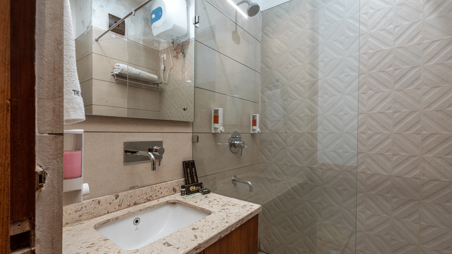 Side view of a bathroom showcasing a mirror above a washbasin with a wooden cabinet beneath and a shower space in the background at DLS The Classio